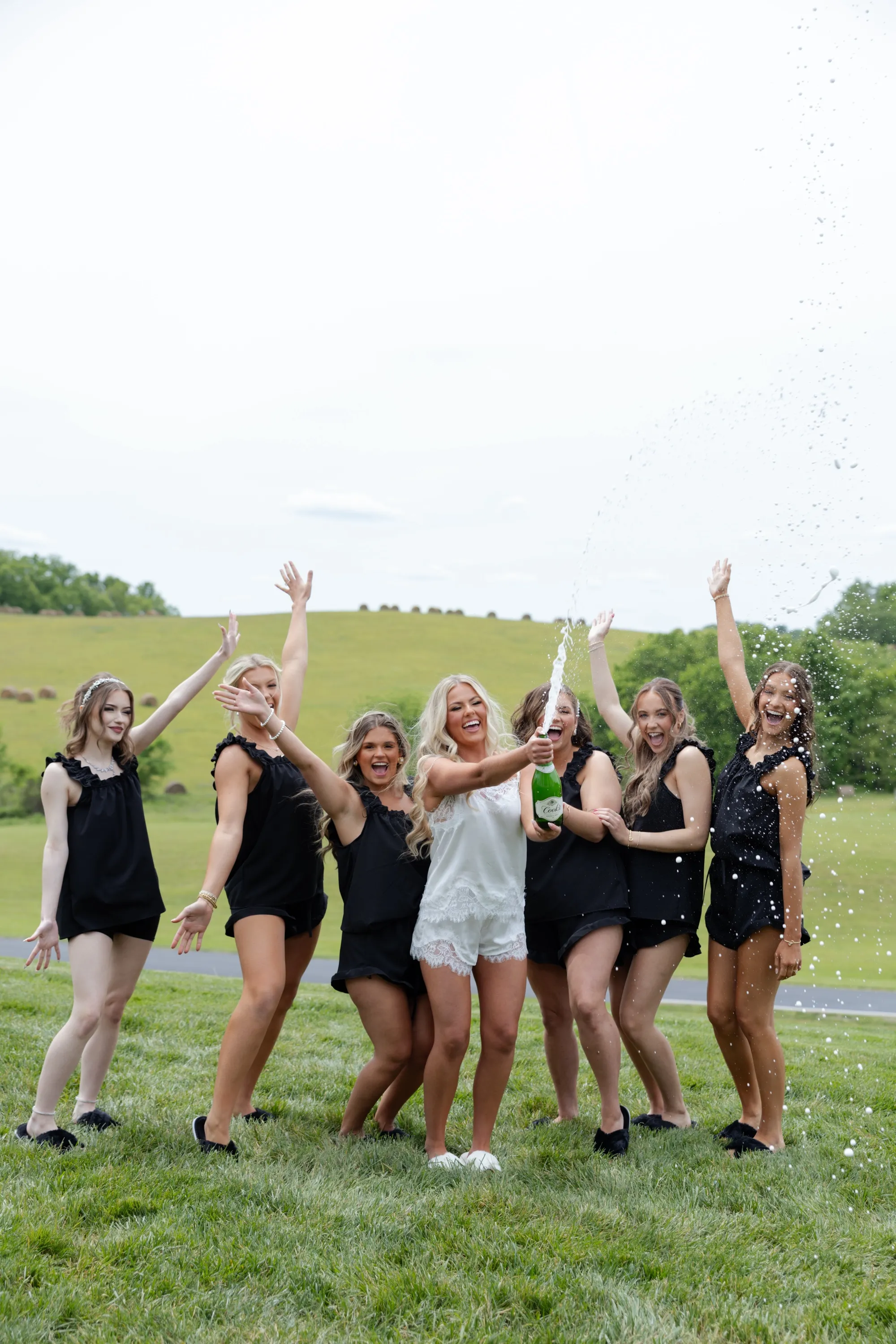 Taylor pops champagne on the lawn with her bridesmaids in black