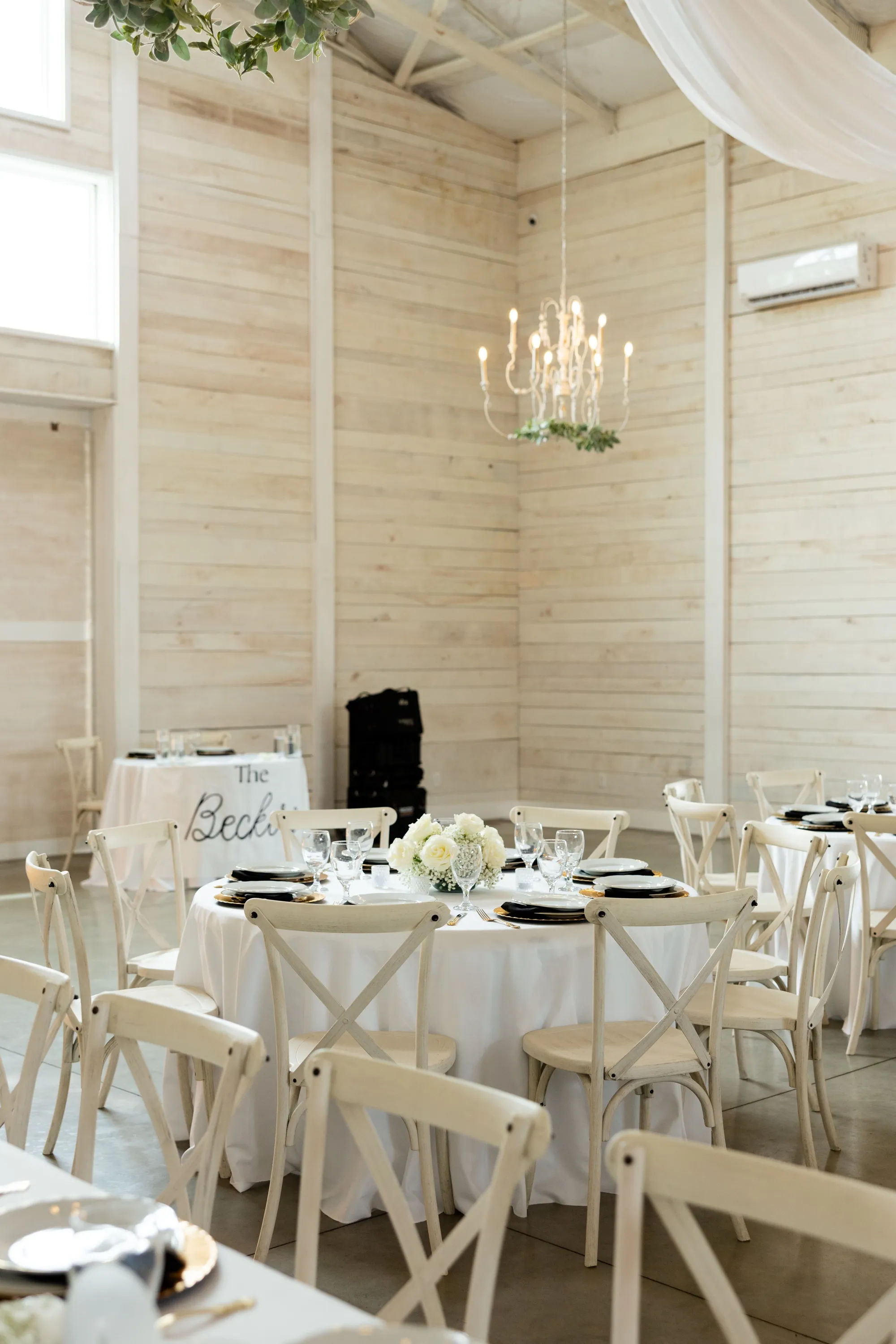 Round tables in white linen with black place settings inside the whitewashed barn
