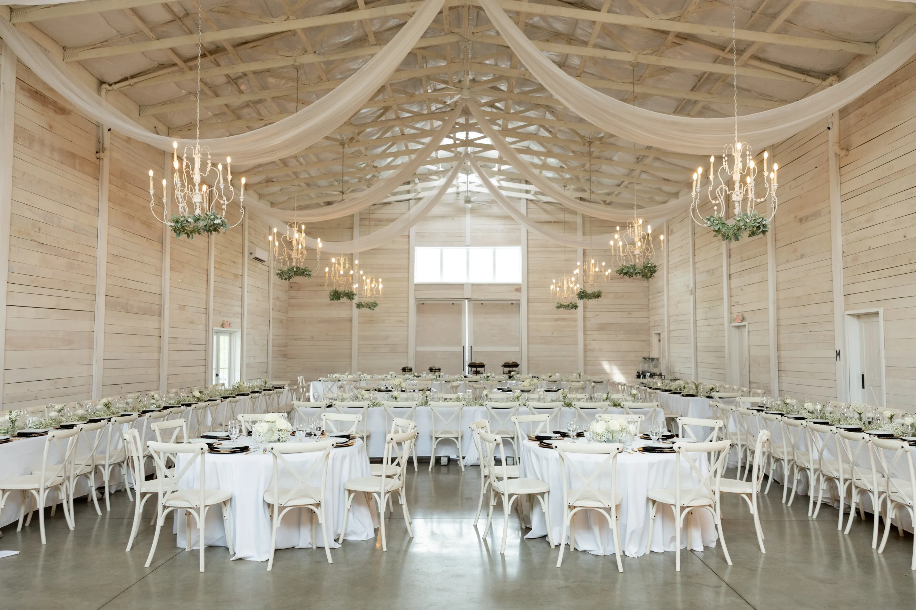 The reception barn set for dinner — draped ceilings, chandeliers, and greenery
