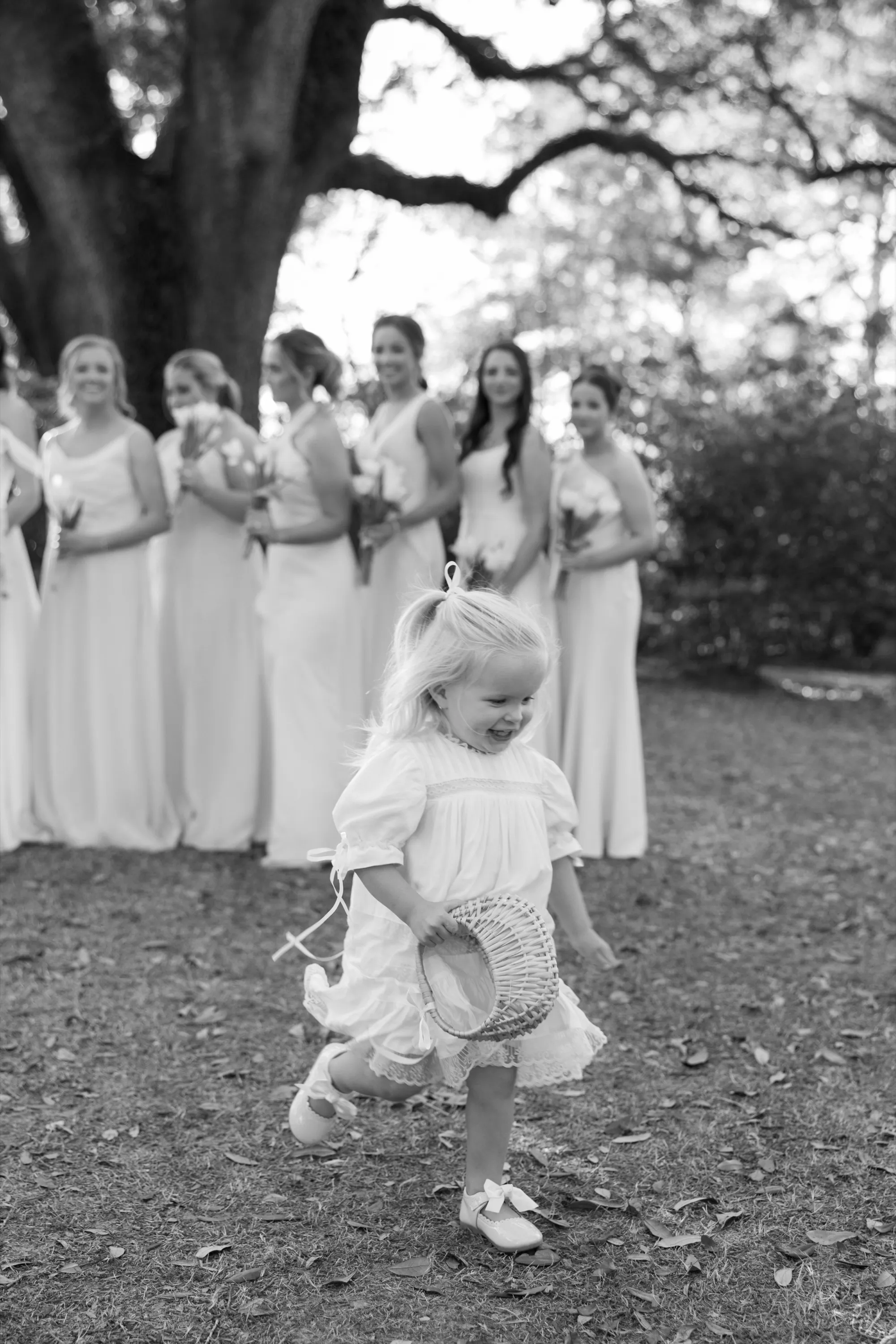 A flower girl at full speed, the bridesmaids behind her, in black and white