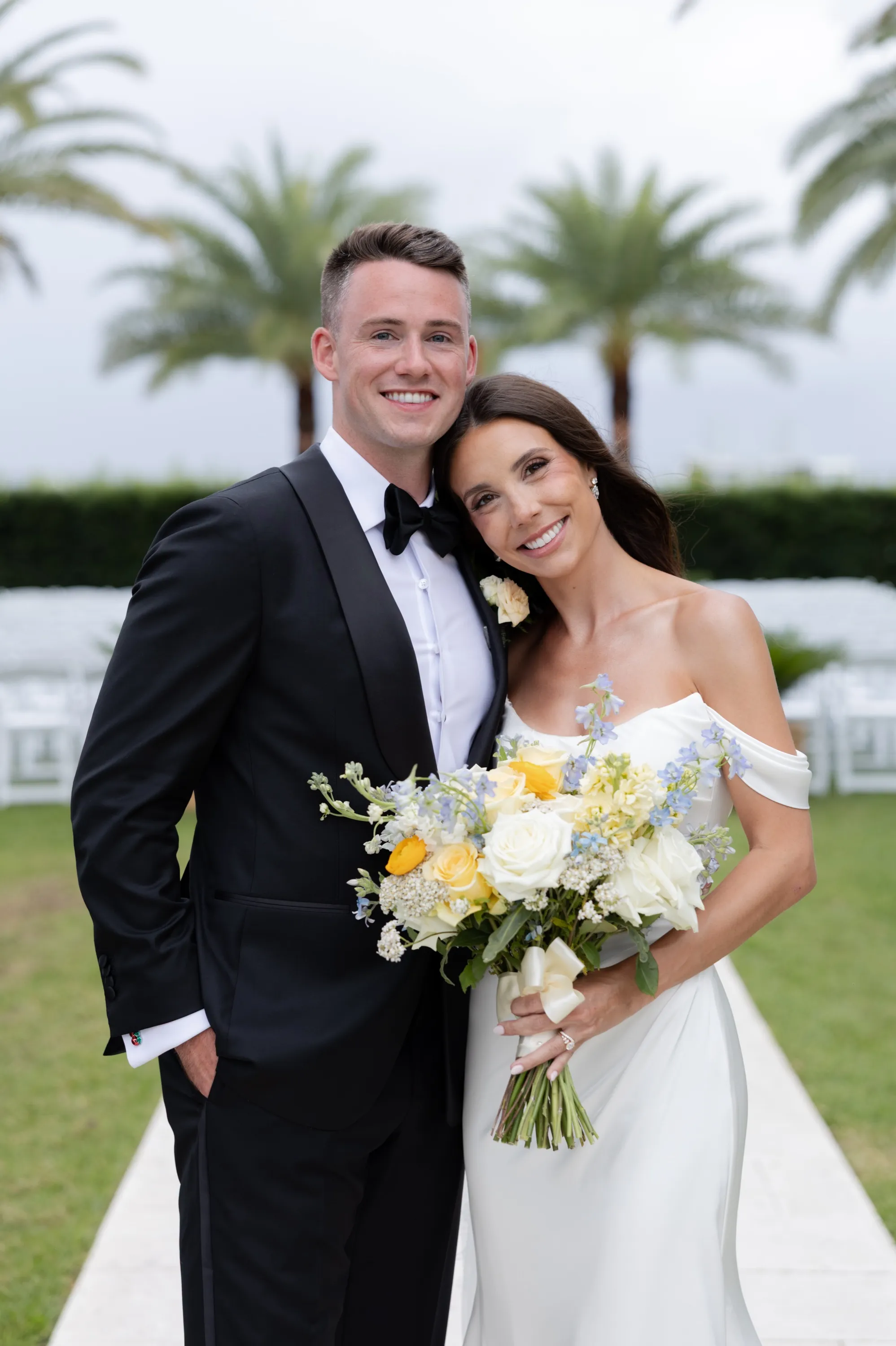 A portrait between the palms, the blue-and-yellow bouquet in hand