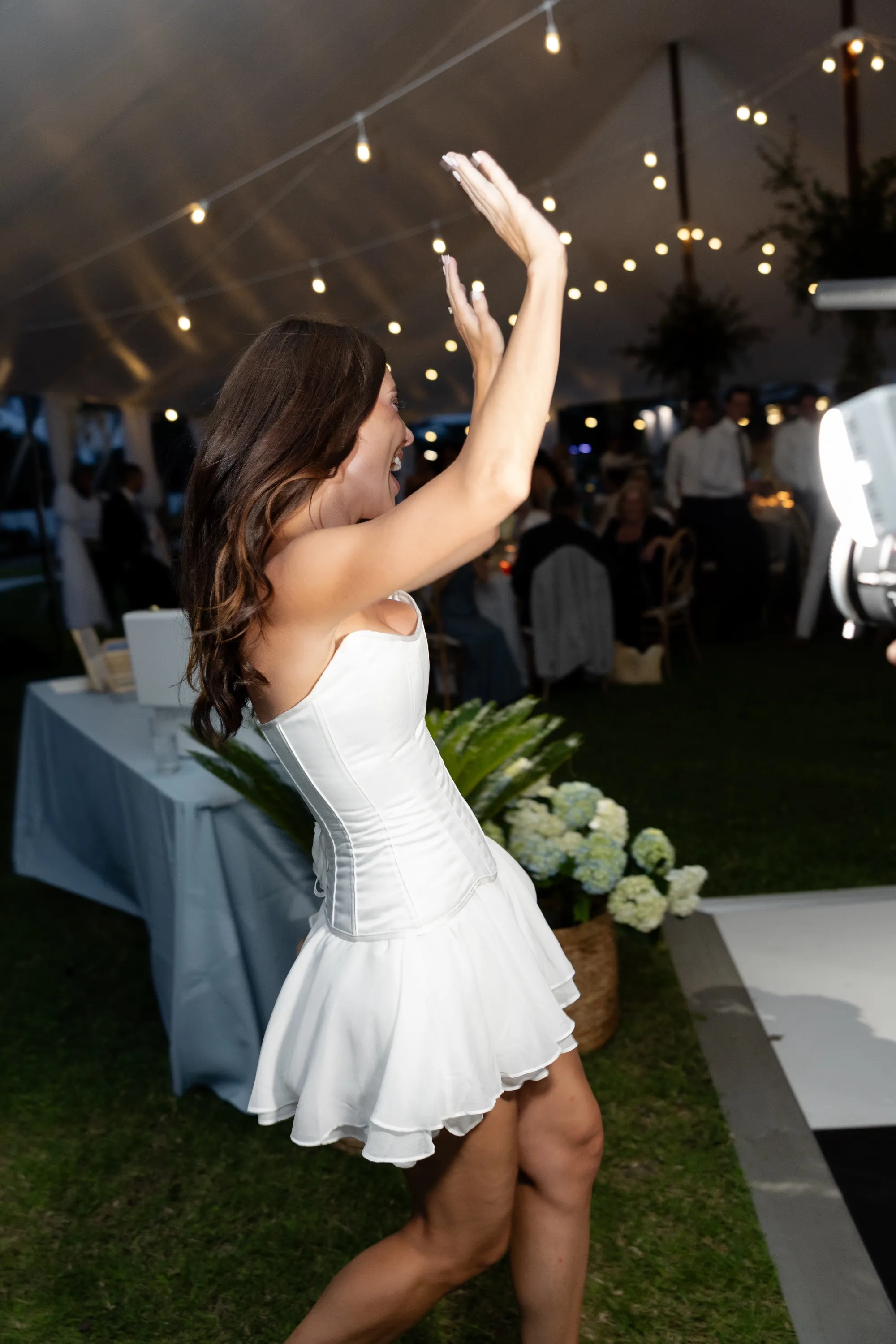 Savannah in her party dress, arms up under the string lights