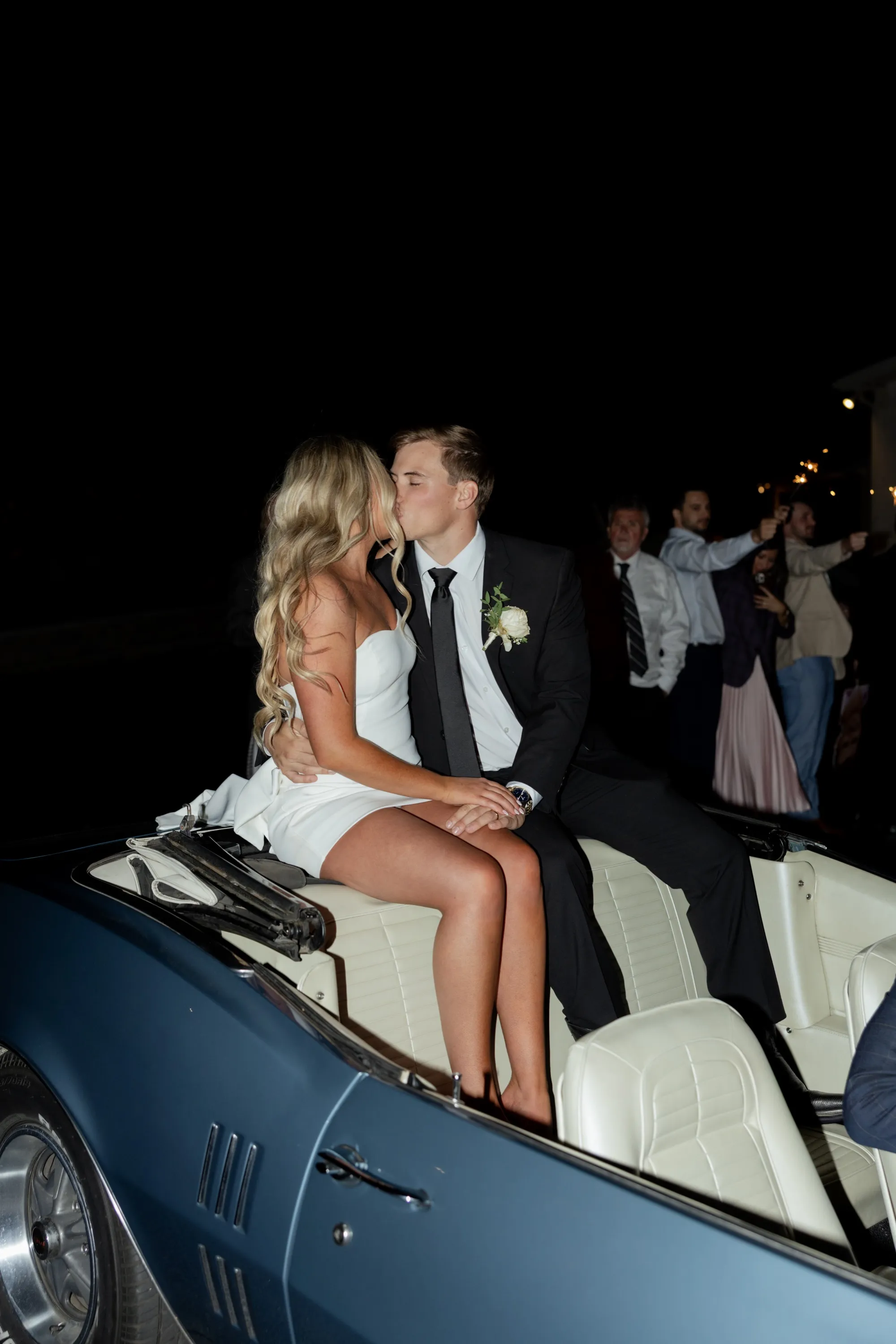 The send-off — arms raised from the back of a vintage blue convertible outside the barn