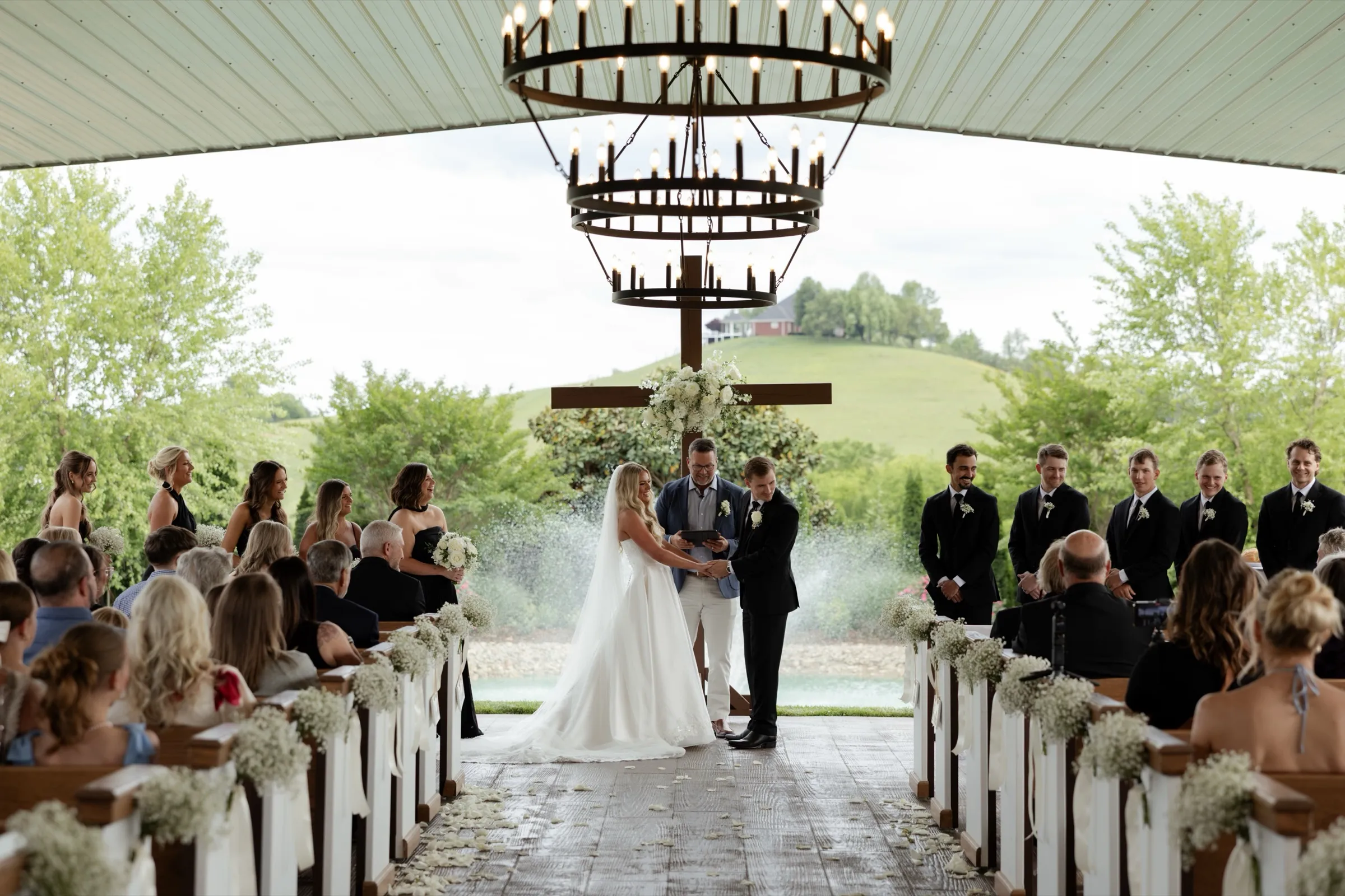 Vows at The White Dove Barn's open-air chapel, the pond and hillside behind the couple
