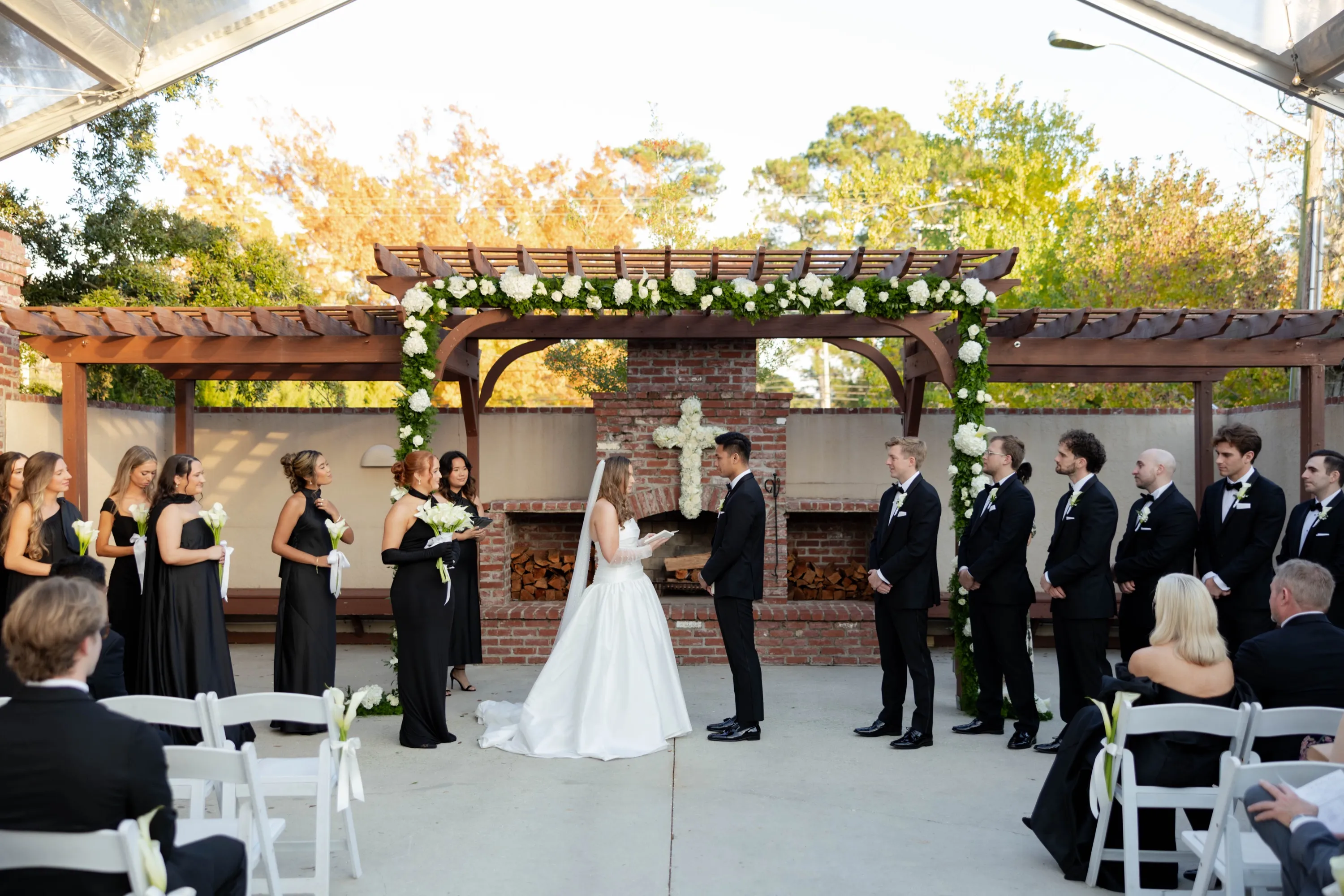 Lily and Edgar's vows under the pergola in the brick courtyard, the wedding party in black around them