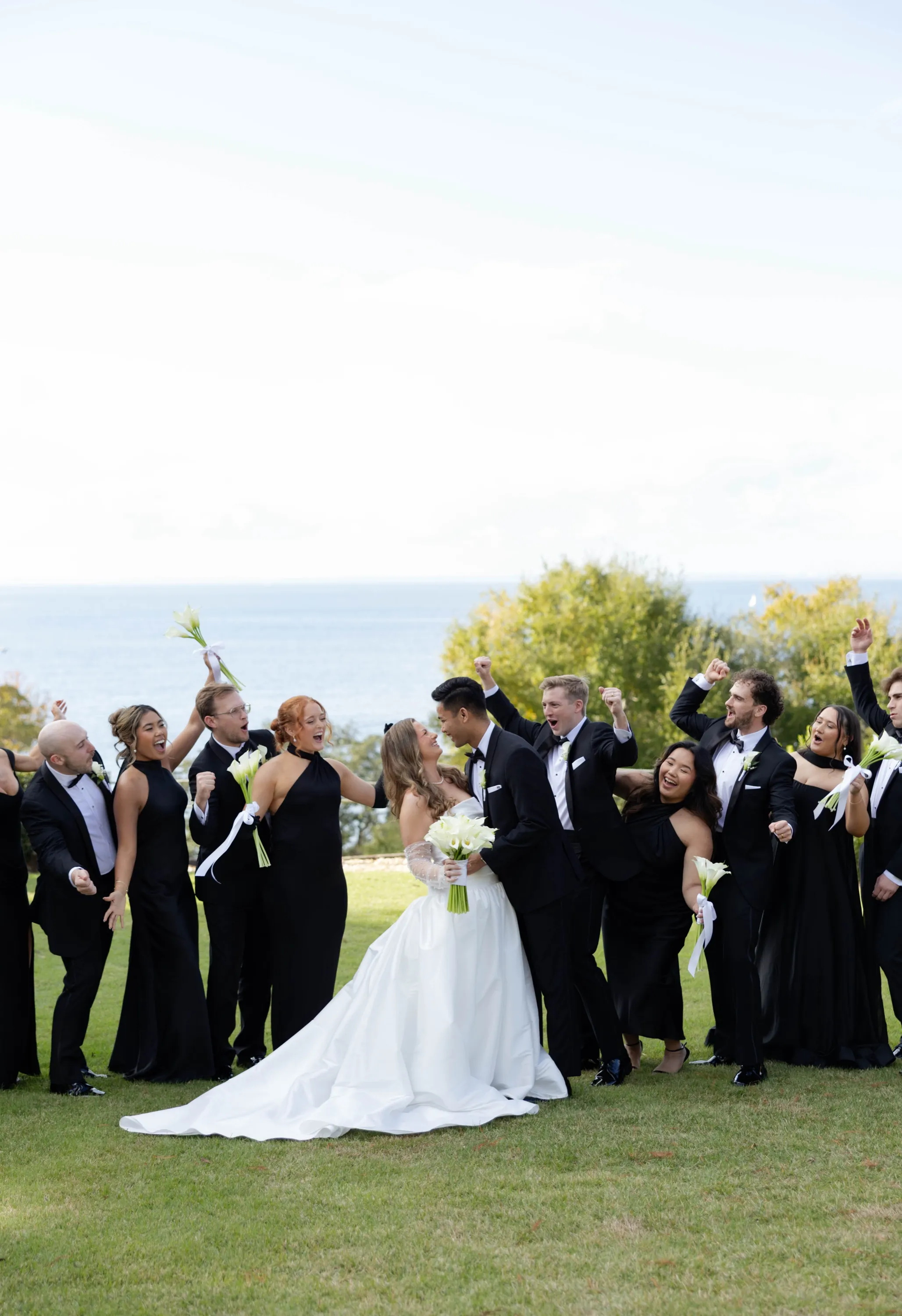 The wedding party in black cheering around the couple above the bay