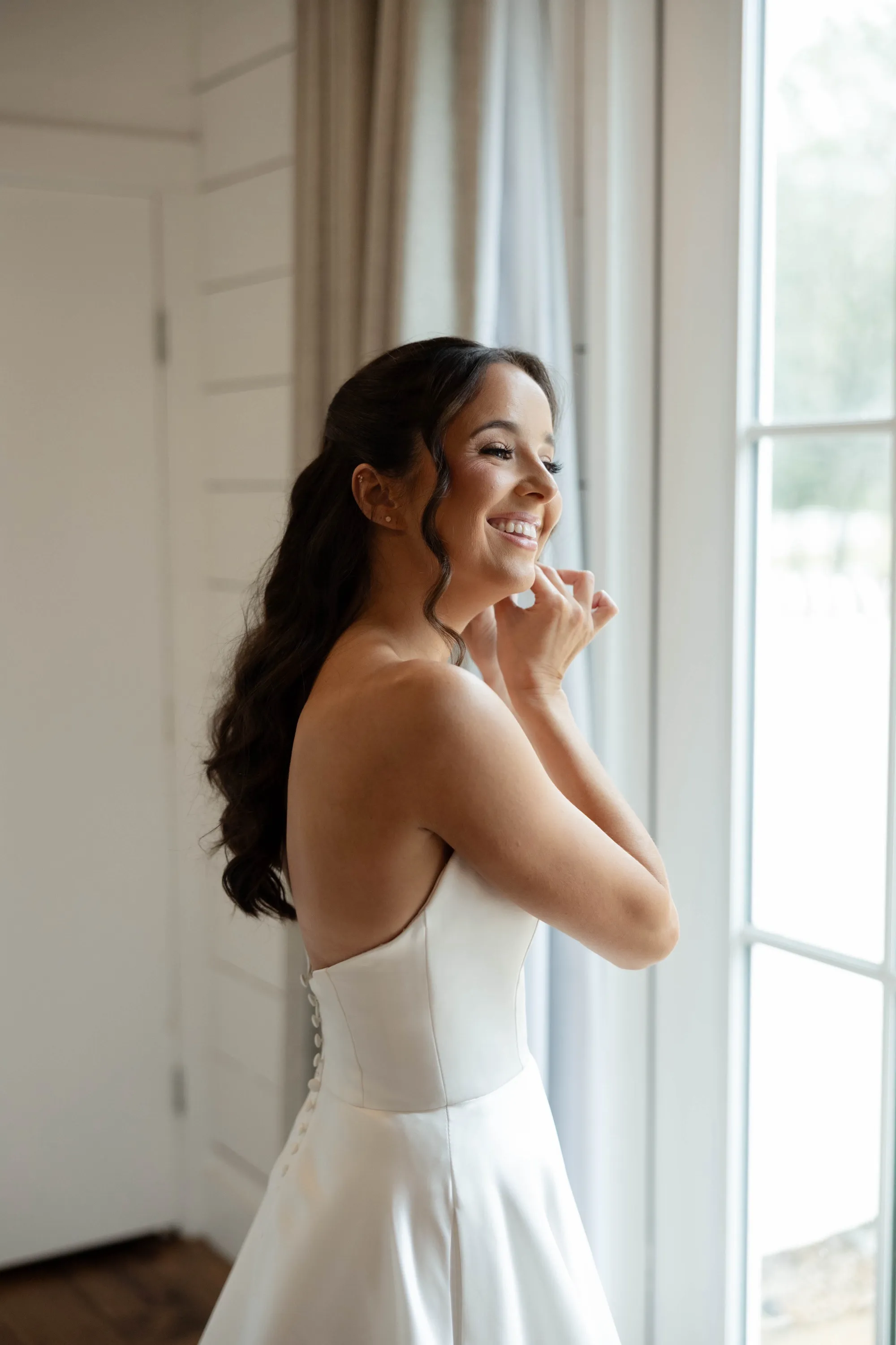 Shelbie smiling at the window as she puts on her earrings