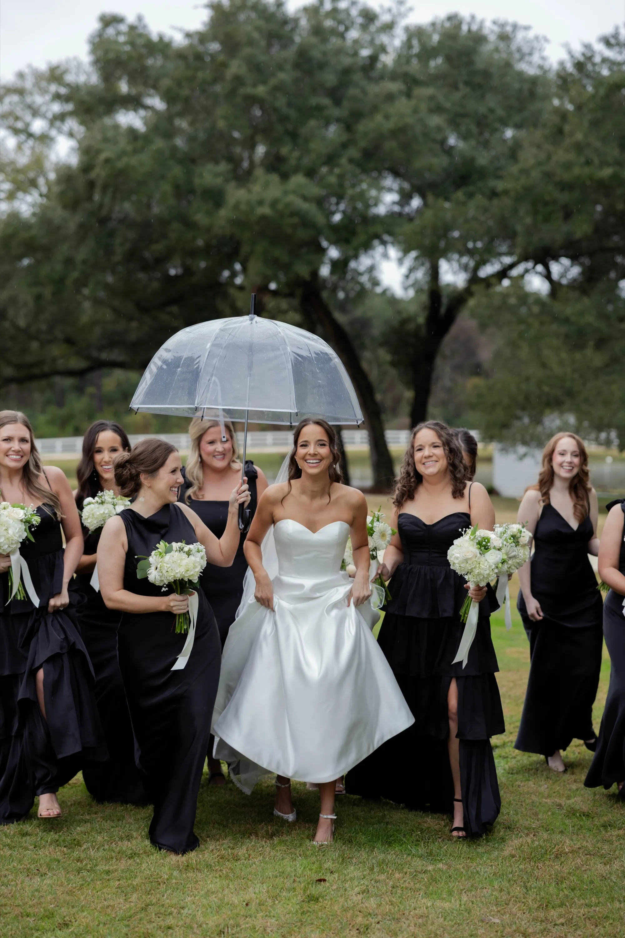 Shelbie under a clear umbrella, her bridesmaids in black around her in the rain