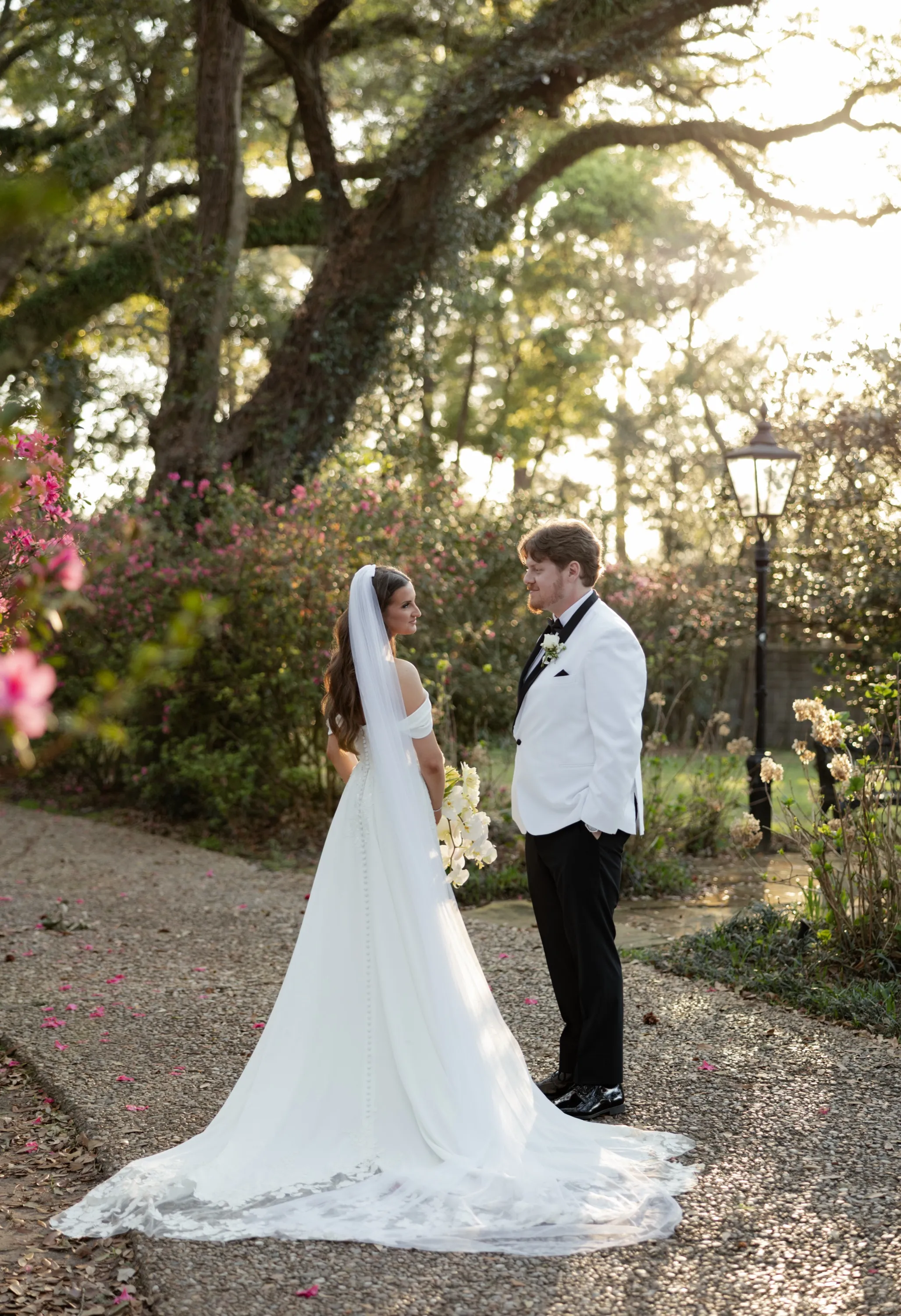Hallie and JT face each other on the garden path at the Bragg Mitchell Mansion, azaleas blooming around them