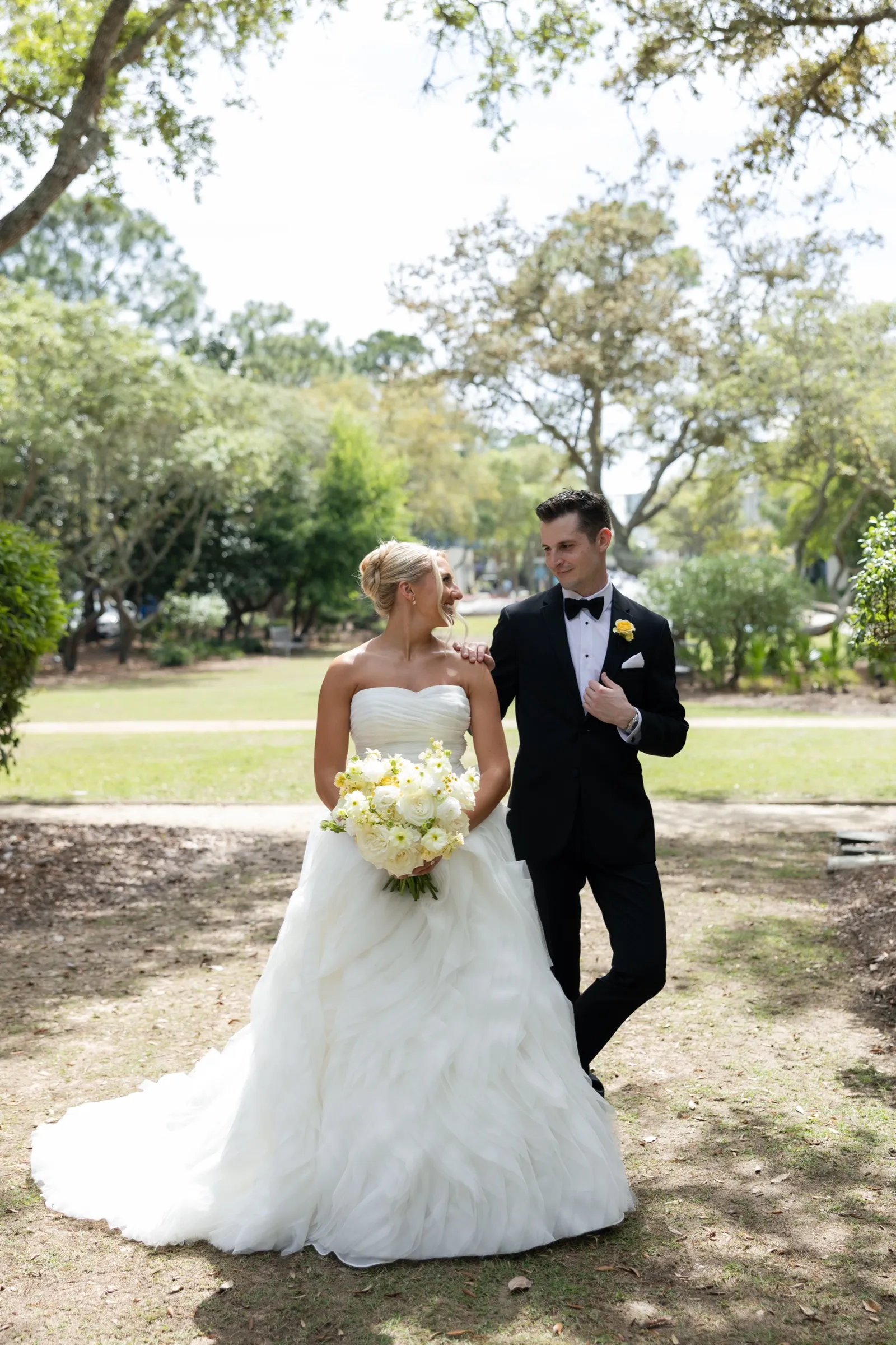 The couple alone under the oaks at midday, her bouquet of white garden roses between them