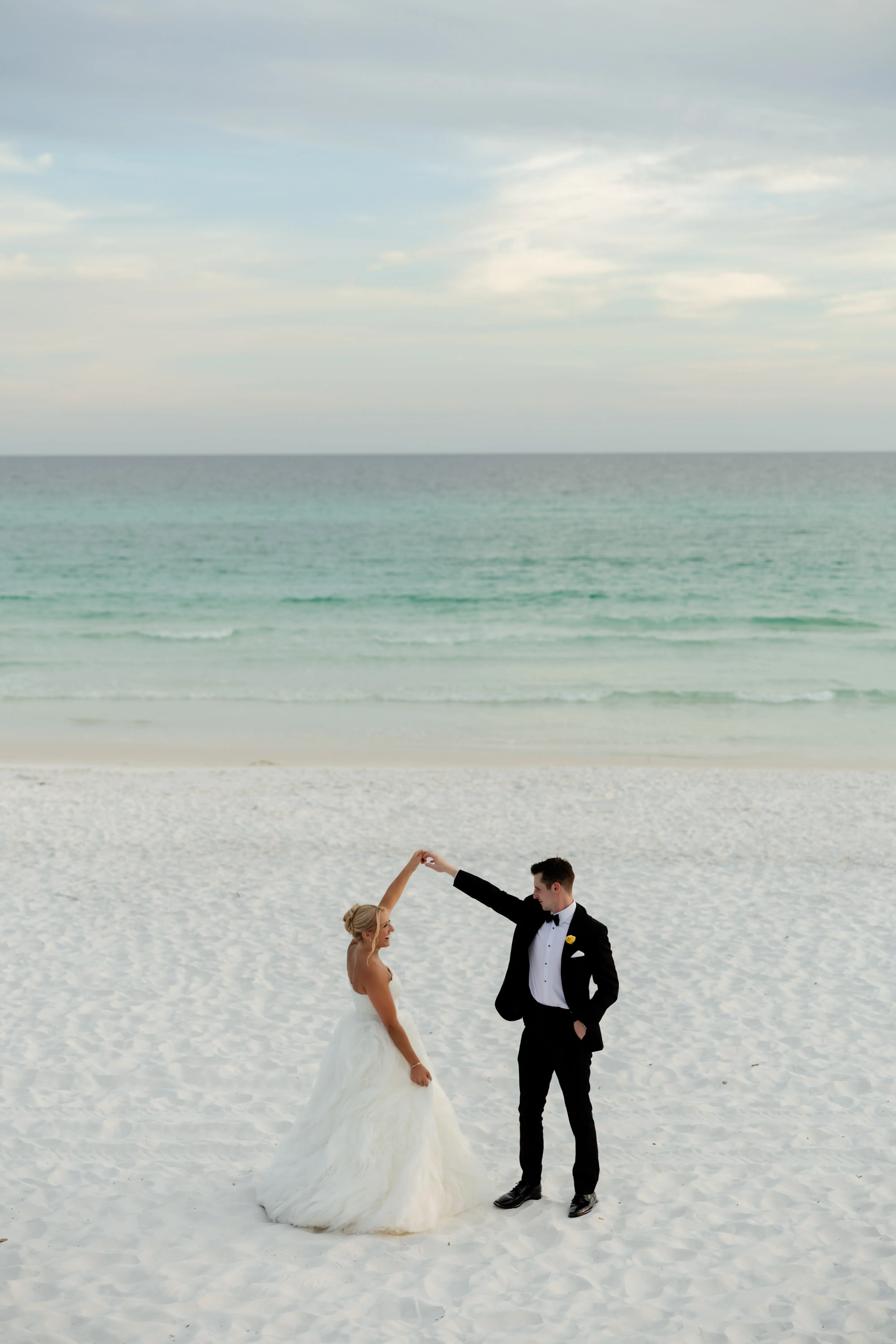 A couple dancing barefoot on white sand with the gulf behind them