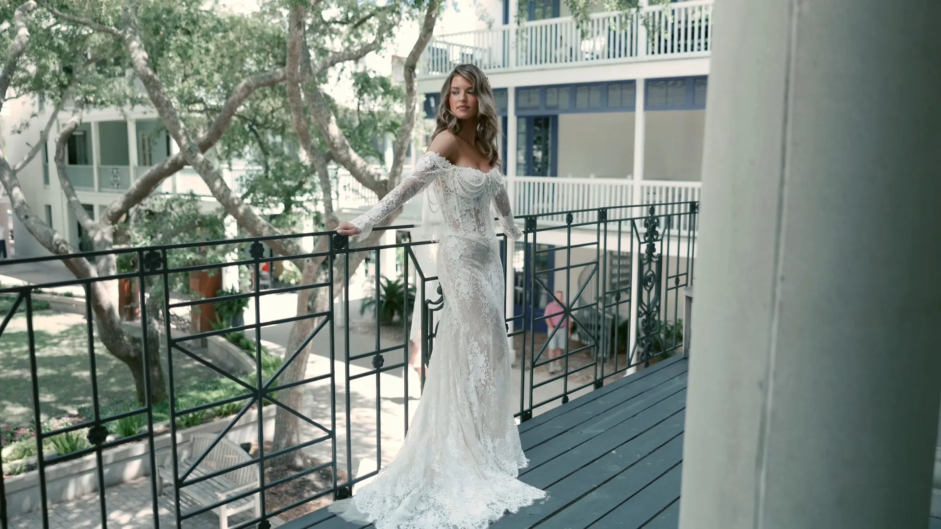 Ivy in her lace gown against the balcony railing, looking back over her shoulder — a frame from the wedding film